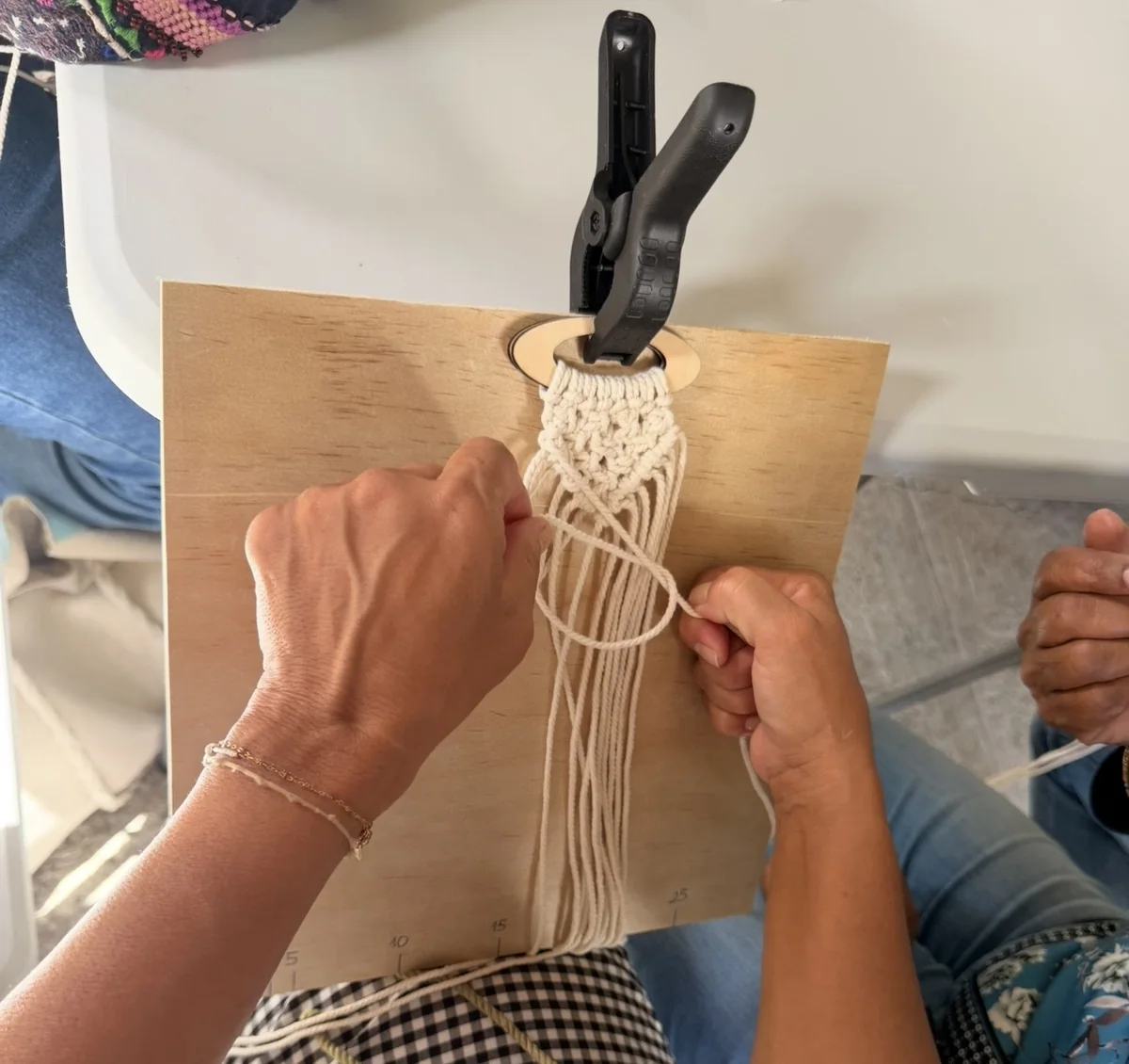 Des mains nouant un macramé sur une planche d’atelier, pendant un atelier Créa-Sens