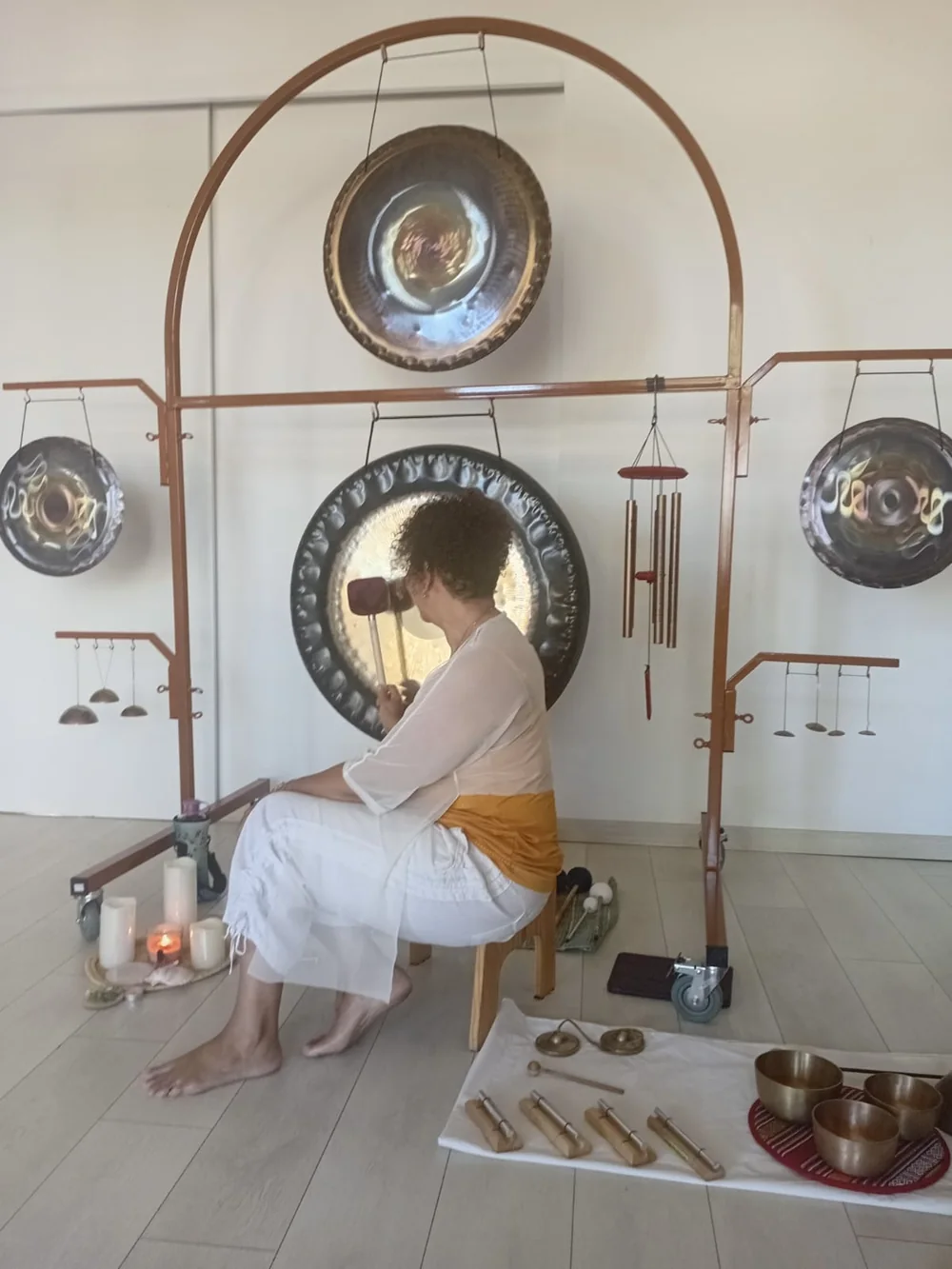 Pascaline en séance, assise de profil devant le grand gong, maillet en main, bougies allumées en soirée
